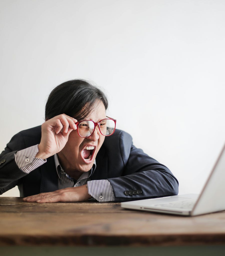Modern Asian man in jacket and glasses looking at laptop and screaming with mouth wide opened on white background